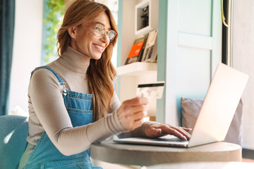 Photo of smiling mature woman holding credit card while using on laptop