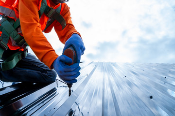 Close up photo of Professional and qualified roofer in protective uniform wear use electric drill to install the metal sheet on the new roof of new modern building construction. © visoot