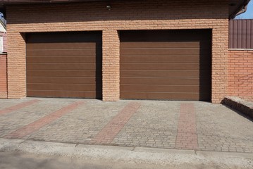 facade of a brown brick garage with two metal gates on a stone pavement on the street on a sunny day
