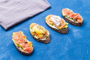 Sandwiches with smoked salmon, eggs, sauce and avocado on blue background. Concept of breakfast and healthy nutrition.
