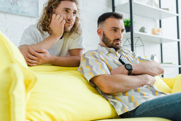 selective focus of displeased homosexual men watching movie in living room