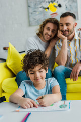 selective focus of happy mixed race kid drawing near homosexual parents