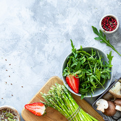 Ingredients for cooking on a gray concrete background. A bunch of fresh green asparagus, strawberries, mushrooms, arugula. Top view. Copy space