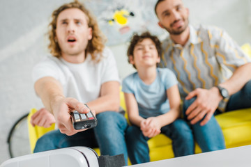 selective focus of homosexual parents and mixed race kid watching tv