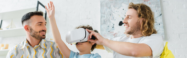 panoramic shot of happy homosexual parents near mixed race son in virtual reality headset