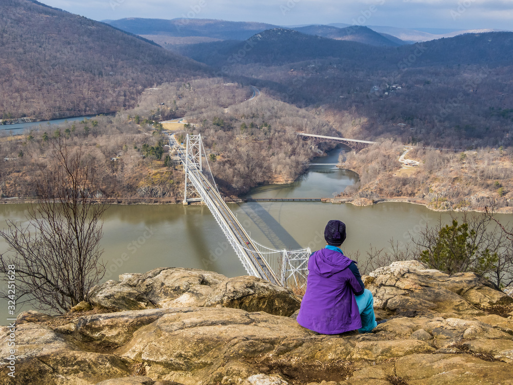 Wall mural Hiker is sitting on the cliff of Anthony's Nose over the Hudson River in Upstate New York