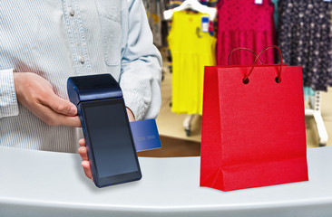 Payment by card purchase in a women's clothing store. Modern payment blue terminal and card. Red...