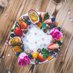 Sweet white cheesecake torte with fresh fruits, poppy and rose flowers on wooden table background