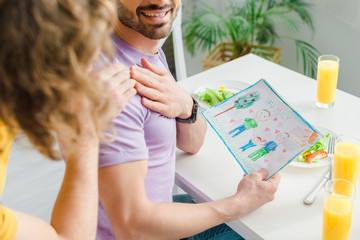 cropped view of homosexual men holding hands near picture with family lettering