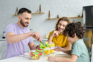 happy homosexual man putting salad on plate of mixed race son