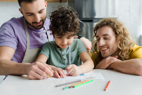 selective focus of mixed race kid drawing near happy homosexual parents