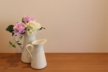 ミルクピッチャーに飾った薔薇と白い壁の背景