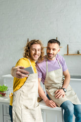 selective focus of happy homosexual men in aprons taking selfie