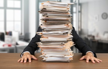 Young businessman hid behind with stack of papers on wooden table - Powered by Adobe
