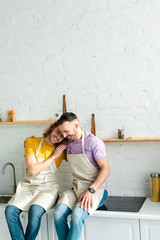 happy homosexual men in aprons smiling in kitchen