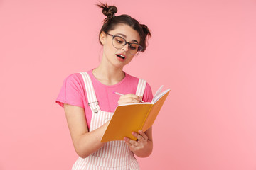 Photo of serious charming girl in eyeglasses writing in exercise book