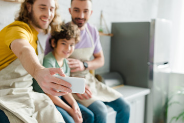 selective focus of happy homosexual men taking selfie with cute mixed race son