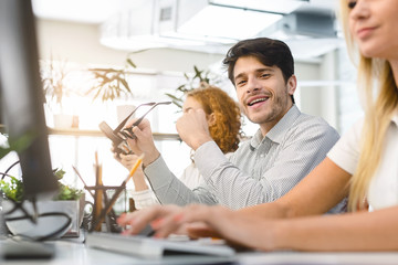 Obraz premium Young man holding glasses while working with business team