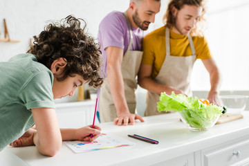 selective focus of mixed race kid drawing with color pencil near homosexual parents
