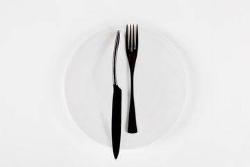 White ceramic round plate  with black cutlery isolated on white.