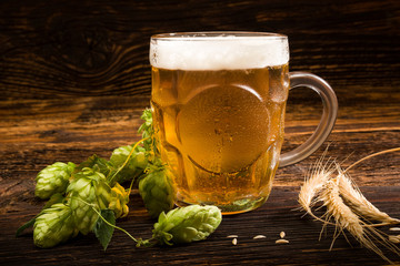 Glass of beer with hops and wheat on vintage wooden background.