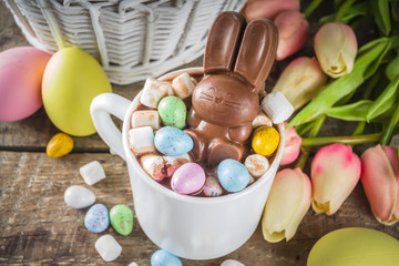 Easter hot chocolate with chocolate bunny rabbits. easter eggs and marshmallow, wooden background with spring flowers copy space