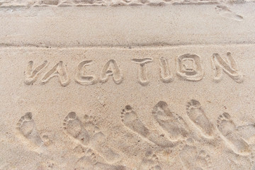 The inscription vacation in the sand on beach and footprints