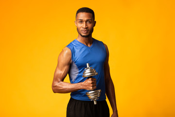 African bodybuilder pumping up biceps with dumbbells at gym