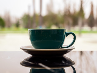 A green Cup with a warming drink on the background of a light window with a copy of space. Reflection of the Cup in the dark surface. Hot chocolate on the table in the coffee shop