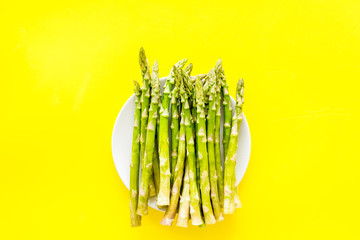 Fresh asparagus on plate on yellow background top-down copy space