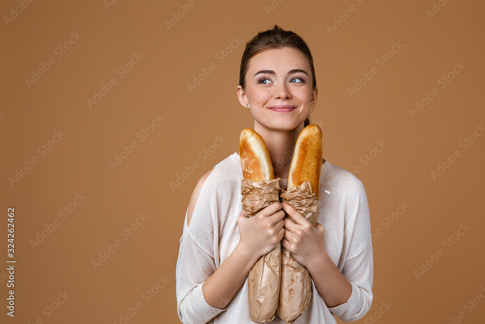 Wall mural portrait of beautiful smiling young woman holding paper bag with bread on studio yellow background. 