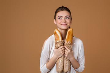 Portrait of beautiful smiling young woman holding paper bag with bread on studio yellow background. girl with paper bag with fresh fragrant long loaf. copy space - Powered by Adobe