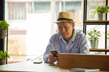 Close up healthy Asian man in light blue shirt and brown hat sitting and watching smart phone to...