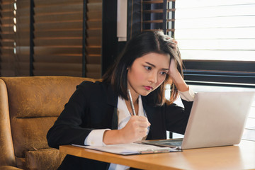 Close up charming young Asian woman in black suit sitting and serious face while working with...