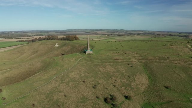 Aerial view panning a monument situated on top of a hill in the English countryside, with a chalk white horse in the background.
The shot was taken on a bright sunny autumn day.