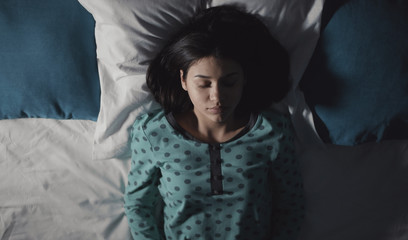 Portrait of dark-haired girl in pajamas lying on back sleeping in bed, half-body picture, top view