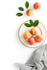Summer lunch. Red peaches on white background with tablecloth and leaves top-down copy space