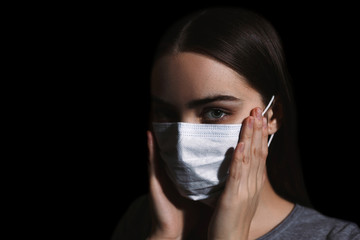 Portrait of young brunette woman wearing medical mask and having illness coronavirus and looking at camera on black background at studio
