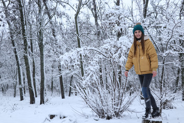 Beautiful girl in a yellow jacket, jeans and a green hat on the snow. Snowy weather, everything in the snow is white. Snowflakes.