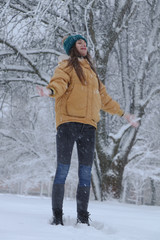 Fototapeta na wymiar Beautiful girl in a yellow jacket, jeans and a green hat on the snow. Snowy weather, everything in the snow is white. Snowflakes.