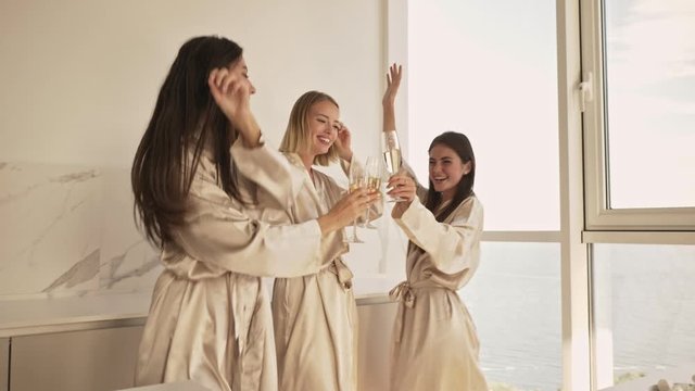 Attractive young girls friends are dancing while holding glasses of champagne in the light bedroom