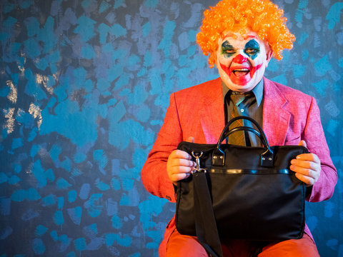 Portrait of male clown in pink dressed for Halloween. actor made makeup from crazy evil clown, faced with bloody smile. White face makeup. Red wig. Model in Halloween costume with black bag
