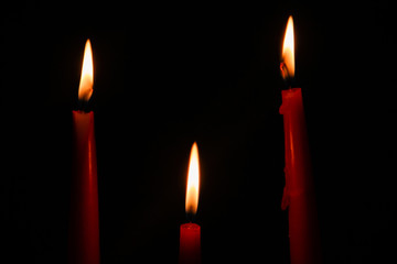 Three red candles on a black background in the dark.