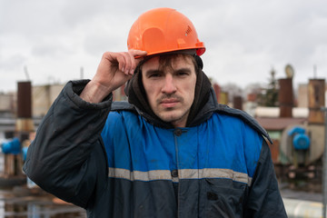 Portrait of a builder in a helmet and working dirty uniform. holds a hard hat. worker on the roof of the factory.