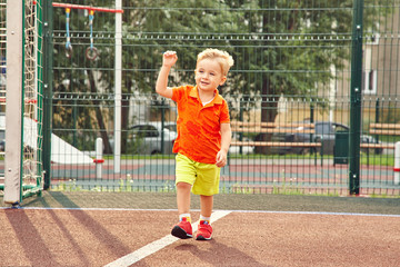 Obraz premium funny little boy on playground with a grid of football gate. playing child on sports ground.