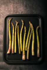  A set of fresh asparagus in a black metal tray on a dark background. Vertical format