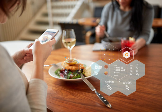new nordic cuisine, technology and people concept - woman with food on smartphone screen and nutritional value chart r at restaurant