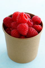 Freshly picked organic raspberries in recycled paper cup. High resolution, light blue background