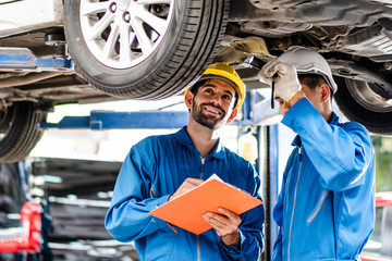 automotive mechanic young men checking under car condition in garage at auto repair shop, assistant...
