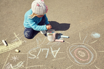 little girl draws chalk on asphalt. child playing in the open air in the summer.